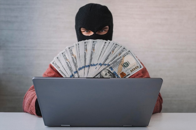 Um ladrão masculino tem dólares na mão usando laptop para atividades de hacking de senha Conceitos de crime cibernético