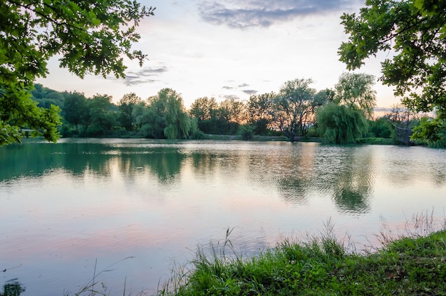 Um lago com árvores e um pôr do sol ao fundo