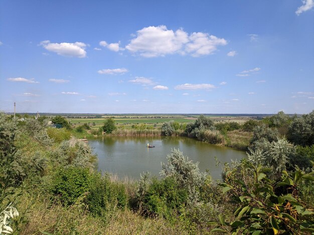 Um lago com um pequeno barco em primeiro plano e um céu azul com nuvens.