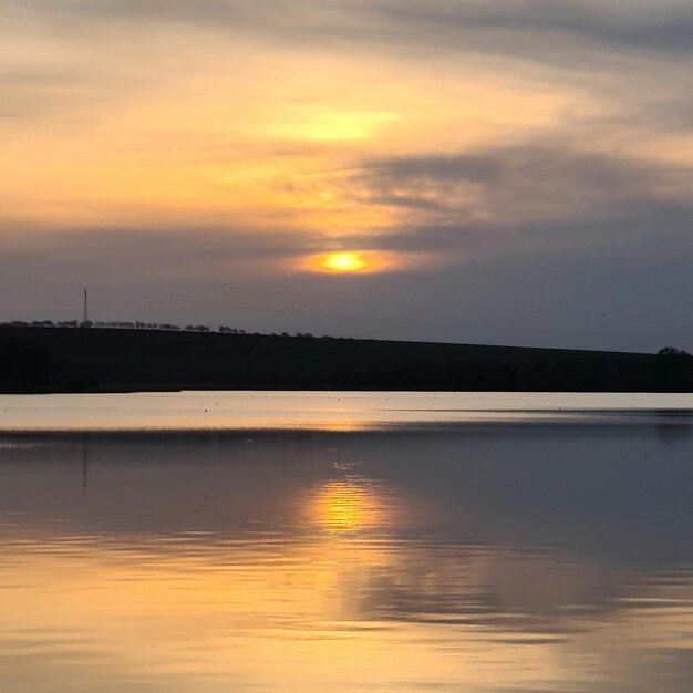 Um lago com um pôr do sol e uma colina ao fundo