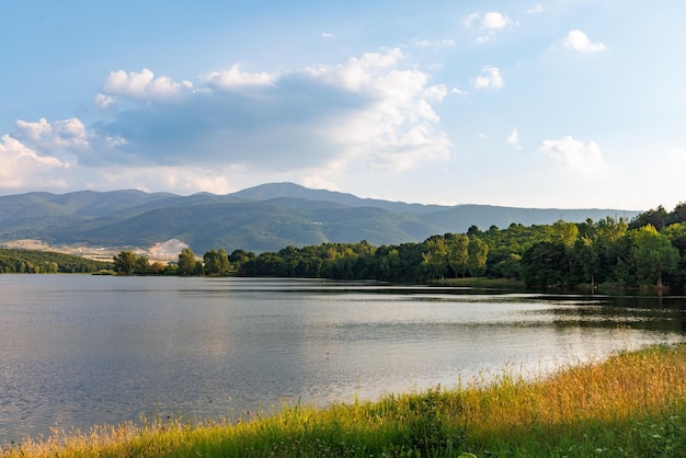 Um lago reflete a luz do sol contra o céu azul e cadeias de montanhas e aldeias