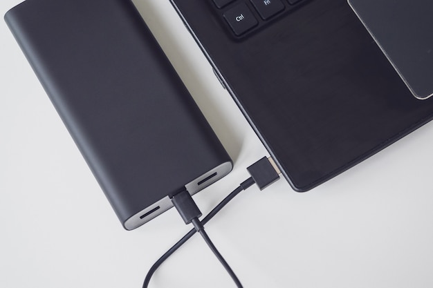 Um laptop aberto é carregado usando um banco de energia por meio de um cabo. dispositivos portáteis modernos.