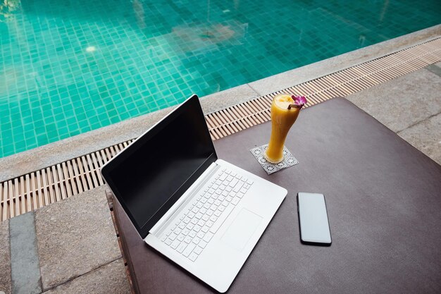 Um laptop móvel e smoothie de manga em uma espreguiçadeira