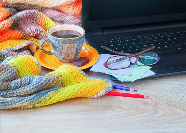 Um laptop uma xícara de café um cobertor de malha e lápis de cor sobre fundo de madeira