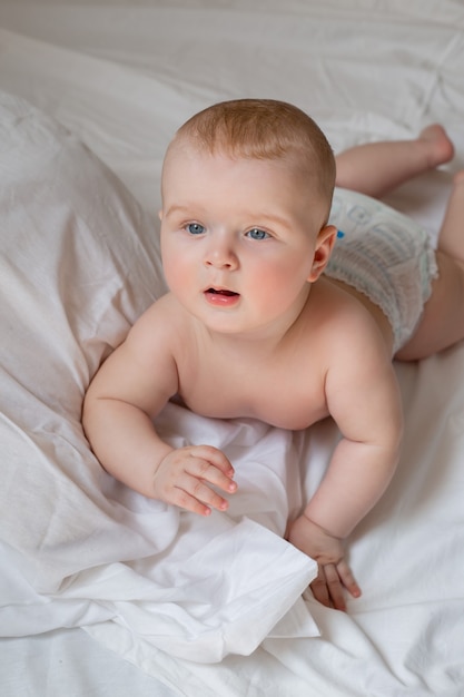 Um lindo bebê está deitado em fraldas em uma cama com lençóis de algodão branco. Foto de alta qualidade