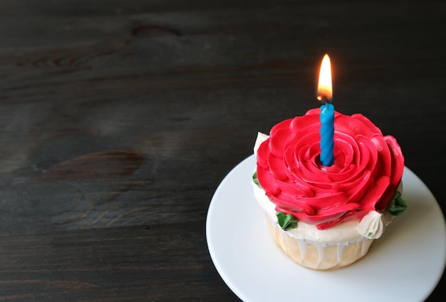 Foto um lindo bolo de aniversário decorado com cobertura em forma de rosa vermelha com uma vela brilhante acesa