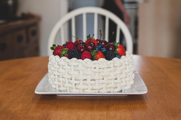 Um lindo bolo de verão decorado com bagas em um prato branco sentado em uma mesa de madeira