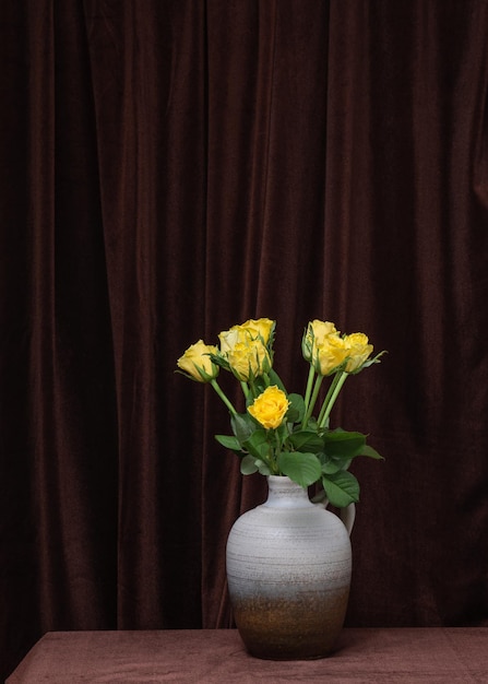 Um lindo buquê de flores de rosas amarelas em um vaso cinza sobre um fundo de tecido marrom escuro Lugar para espaço de cópia de texto