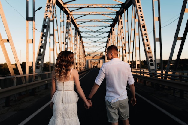 Um lindo casal apaixonado por um homem e uma mulher se beijam em uma grande ponte de metal ao pôr do sol