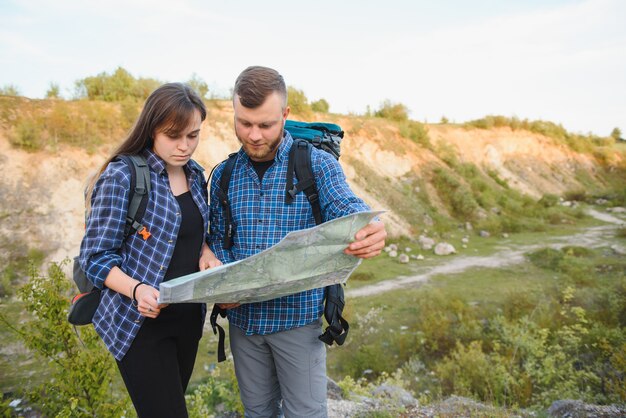 Um lindo casal de viajantes está procurando no mapa de localização enquanto está em uma colina alta em um dia ensolarado