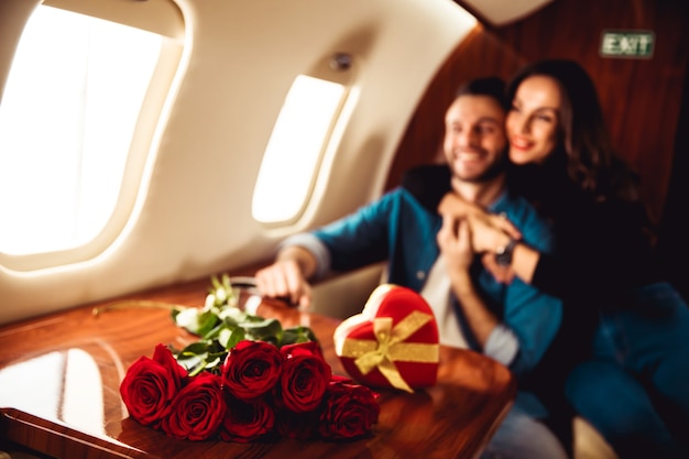 Um lindo casal está comemorando o Dia de São Valentim em um jato particular. Um homem está dando um presente em uma caixa vermelha para sua namorada