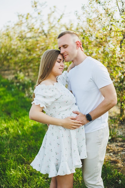 Um lindo casal jovem esperando uma gravidez em um lugar romântico, um pomar de maçãs em flor na primavera Casal feliz e alegre se divertindo enquanto caminhava no jardim Um homem segura a mão de uma mulher