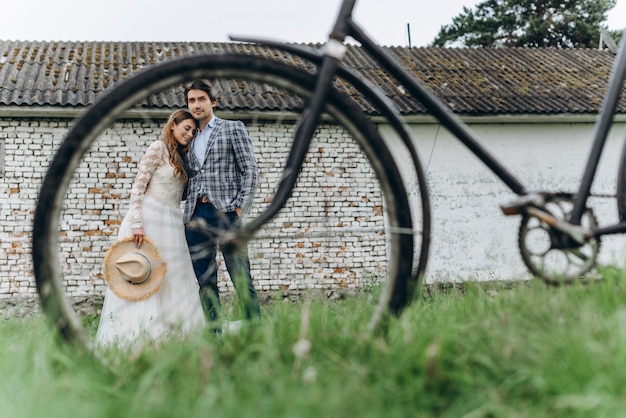 Um lindo casal jovem noiva e noivo com uma bicicleta perto de casa velha