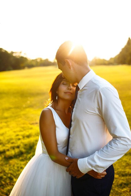 Foto um lindo casal no pôr-do-sol, o noivo e a noiva em trajes de noiva com um buquê de flores, romântico.