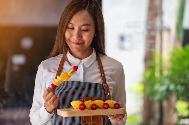 Um lindo chef feminino segurando frutas frescas misturadas em espetos em uma placa de madeira