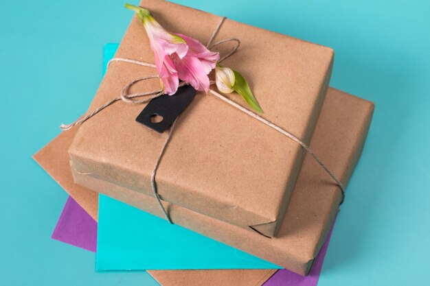 Um lindo e delicado buquê de alstroemeria rosa deitado em um envelope em um fundo azul Presentes embalados em papel kraft ao lado de flores