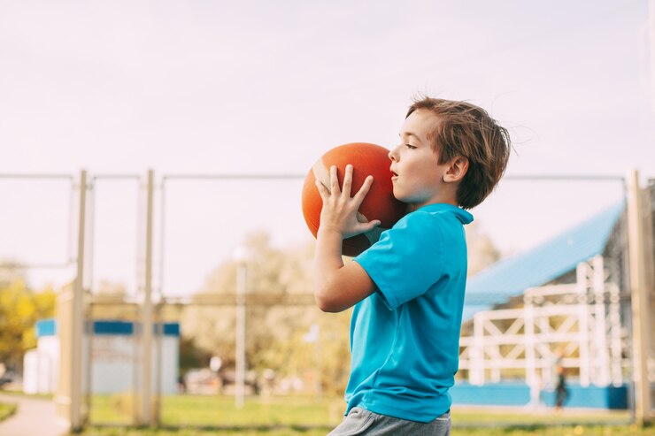 Um lindo garoto em um uniforme esportivo segura uma bola de basquete nas mãos e se prepara para lançar, esporte