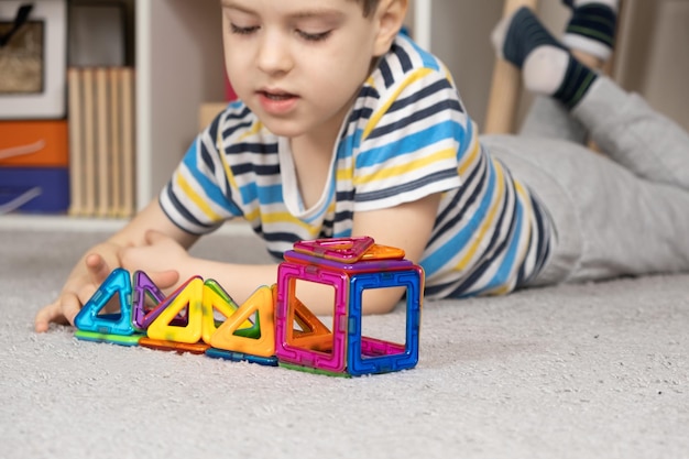 Foto um lindo menino de 5 anos cria figuras com um kit de construção magnético