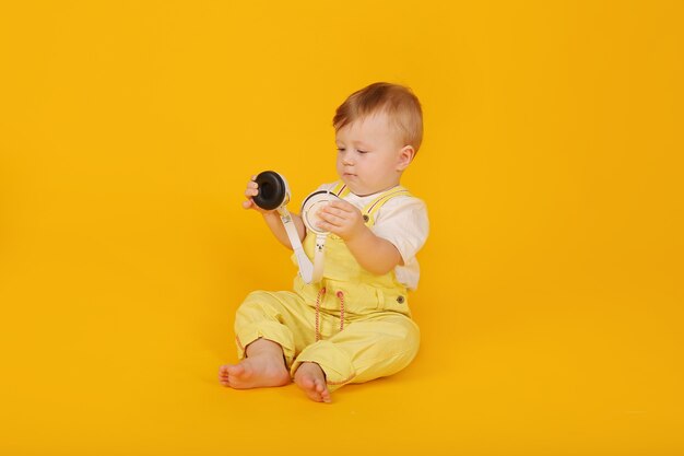 um lindo menino feliz de olhos azuis em um terno amarelo com fones de ouvido nas mãos