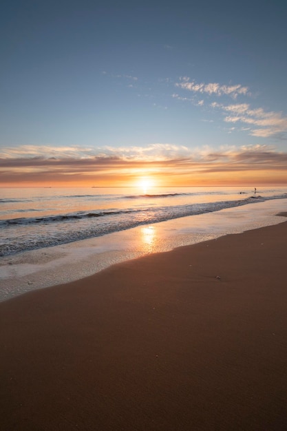 Um lindo pôr do sol na praia de Mazagon Espanha Ao fundo as silhuetas de dois surfistas