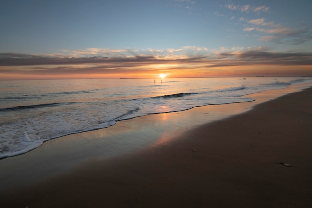 Um lindo pôr do sol na praia de Mazagon Espanha Ao fundo as silhuetas de dois surfistas