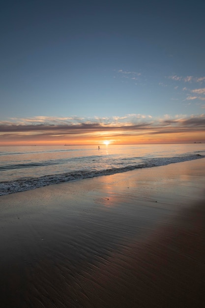 Um lindo pôr do sol na praia de Mazagon Espanha Ao fundo as silhuetas de dois surfistas