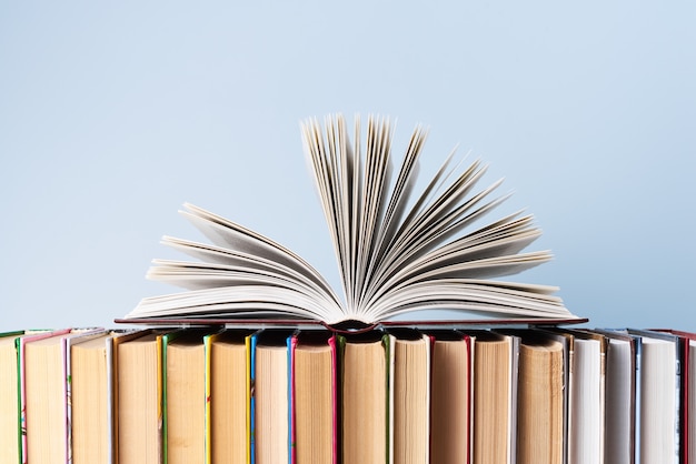 Um livro aberto encontra-se em uma fileira de livros em várias encadernações contra uma parede azul clara