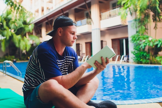 Um livro de leitura do homem ao lado da piscina no jardim.