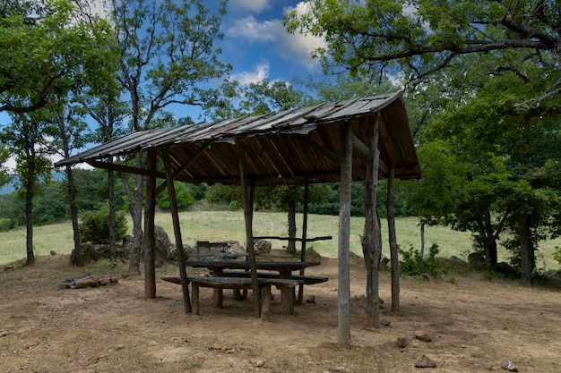 Um lugar de descanso equipado para um piquenique nos bancos de madeira das montanhas e uma mesa sob o telhado contra o pano de fundo de uma paisagem de montanha