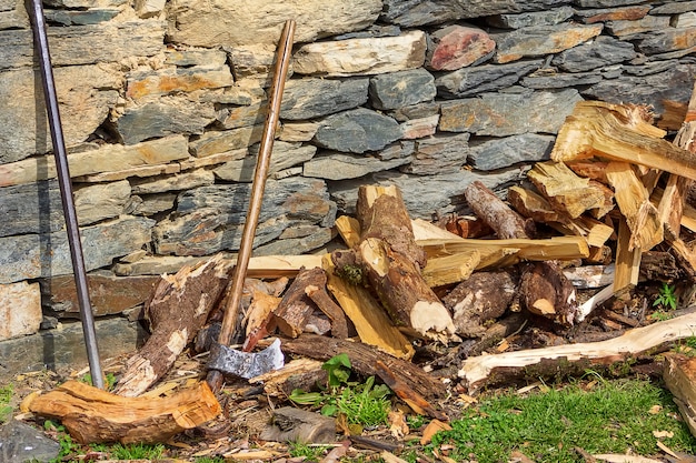 Um machado de madeira e uma vara de metal perto da parede de pedra e lenha picada