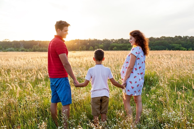 Um marido, sua esposa e um filho estão posando no campo de trigo ao pôr do sol