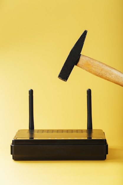 Um martelo atinge o roteador do modem WiFi para quebrá-lo contra um fundo amarelo