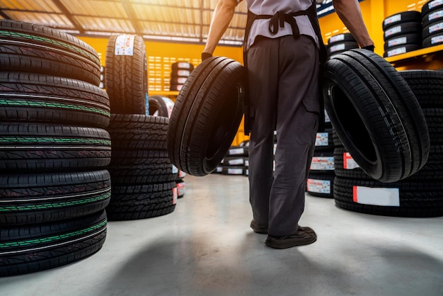 Foto um mecânico de automóveis masculino segurando dois pneus na loja de pneus para armazenamento ou estoque de pneus novos em um grande armazém no centro de serviço ou oficina mecânica para a indústria automobilística