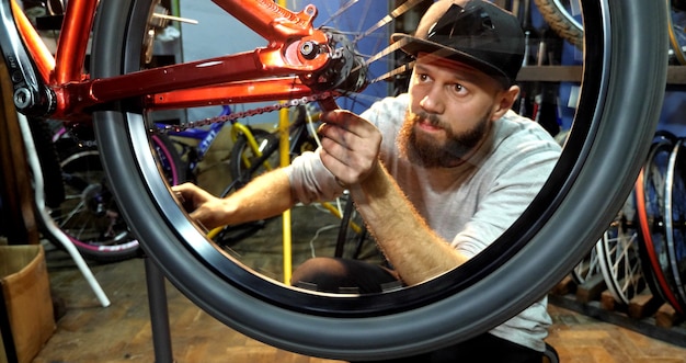 Foto um mecânico de bicicletas com barba monta uma mountain bike em sua oficina.