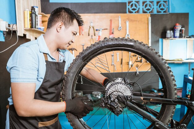 Um mecânico de bicicletas no avental instala os eixos ao instalar as rodas da bicicleta