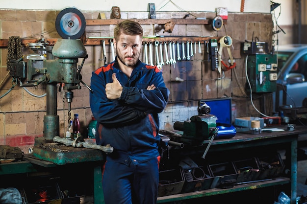 Um mecânico em um traje de proteção azul está parado em uma garagem de carro perto de uma furadeira.