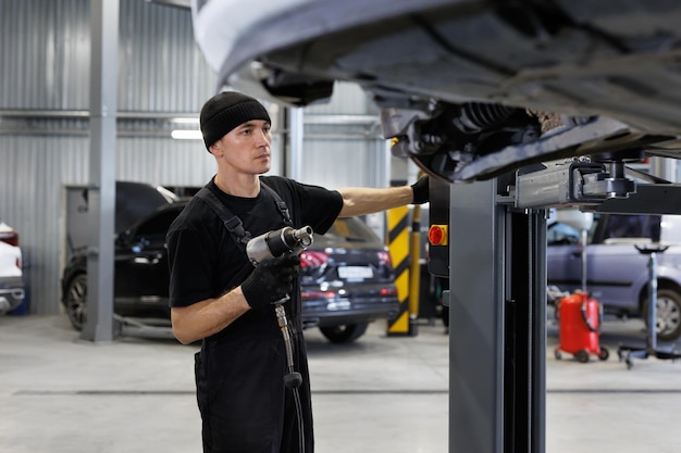 Um mecânico inspecionando ou consertando o rack de direção debaixo do carro em uma oficina de reparo de automóveis