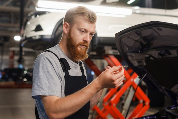 Um mecânico masculino verifica o nível de óleo em uma estação de serviço de automóveis Limpe o espaço moderno de reparação de automóveis