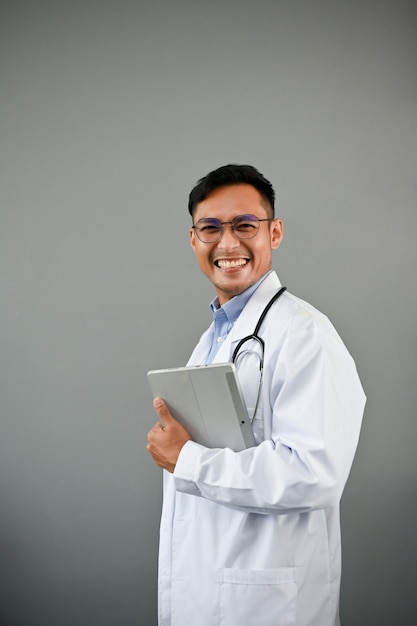 Um médico asiático inteligente de uniforme com estetoscópio está segurando um tablet digital