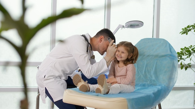 Um médico atencioso examina a orelha de uma menina usando um dispositivo especial
