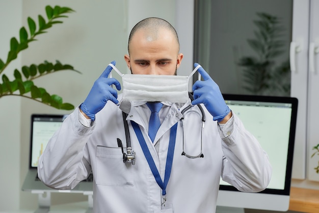 Um médico caucasiano, colocando uma máscara facial em seu escritório.