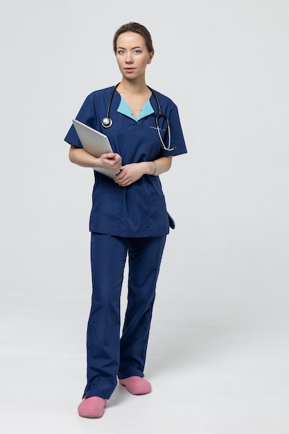 Um médico cirurgião amigável em um terno azul segura um laptop em um fundo branco ajudando as pessoas no hospital