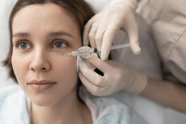 Um médico cosmetologista faz injeções com uma seringa com uma pequena agulha na bochecha do cliente Remoção de rugas faciais