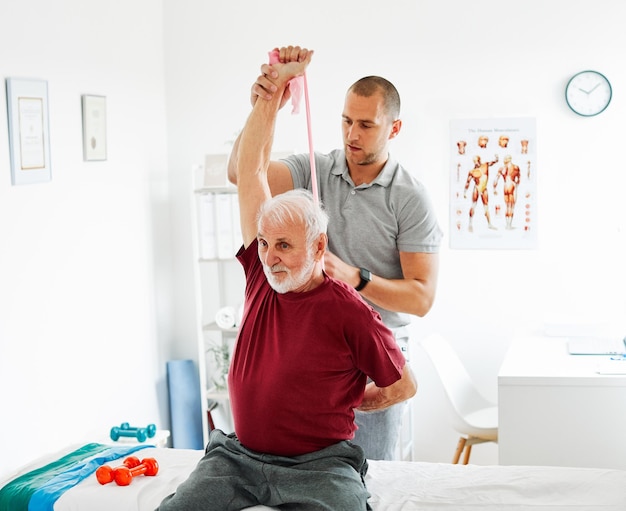 Um médico dá fisioterapia a um homem idoso em casa.