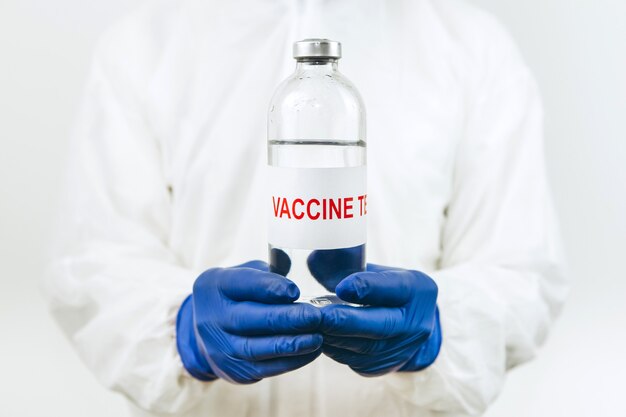 Um médico de jaleco branco e luvas azuis segura um tubo de ensaio de seringa com uma vacina contra o coronavírus. Injeção de vacina Covid 2019. 2020 coronavírus pandêmico. Teste de vacina.