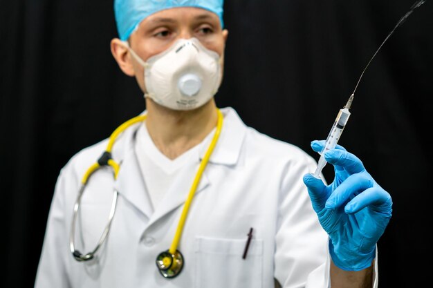 Um médico de jaleco branco e uma seringa na mão Um homem com uma máscara médica e um vestido médico em um fundo preto Vacinação contra coronavírus e covid19