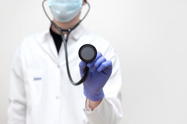 Um médico de uniforme branco segura um estetoscópio na mão contra um fundo branco