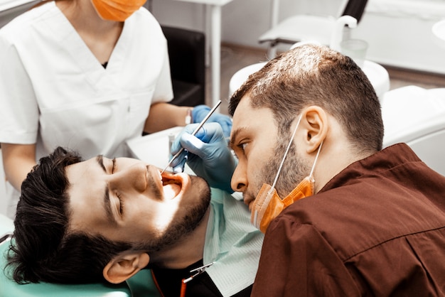 Um médico dentista jovem trata um paciente. Manipulações médicas em odontologia, cirurgia. Uniforme profissional e equipamento de um dentista. Cuidados de saúde Equipando um local de trabalho médico. Odontologia