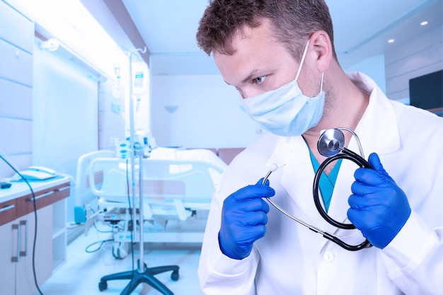 Um médico jovem e bonito, trabalhando em um hospital, com uma bata de médico, uma máscara de pé de lado e segurando um estetoscópio