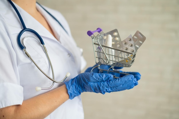 Um médico sem rosto com um jaleco e um estetoscópio segura um pequeno carrinho de compras cheio de medicamentos Conceito de farmácia